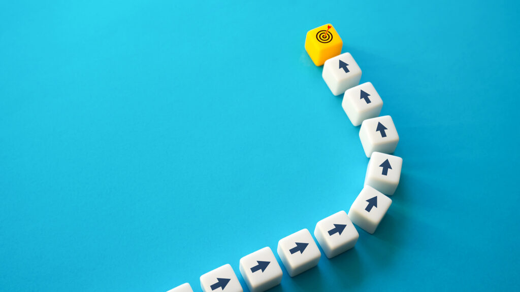 White dice with arrows all moving in the same track and towards the same direction. At the end is a yellow die with a target and arrow hitting the bullseye.